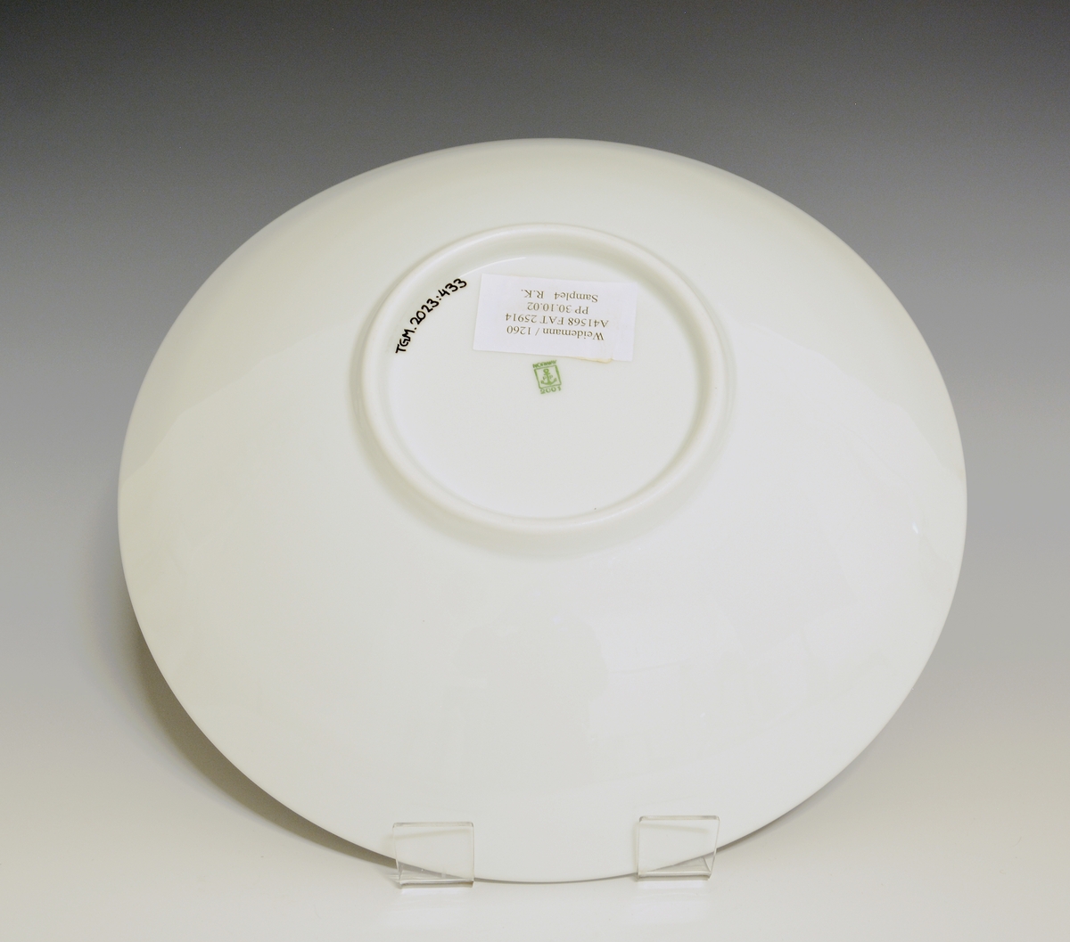 Fat av porselen med hvit glasur. Dekorert med nonfigurativt motiv i blått, gult, grønt og rødt. Jakob Weidemanns signatur på fanen.
Modell: 2591.4
Dekor etter motiv av Jakob Weidemann
Prøve