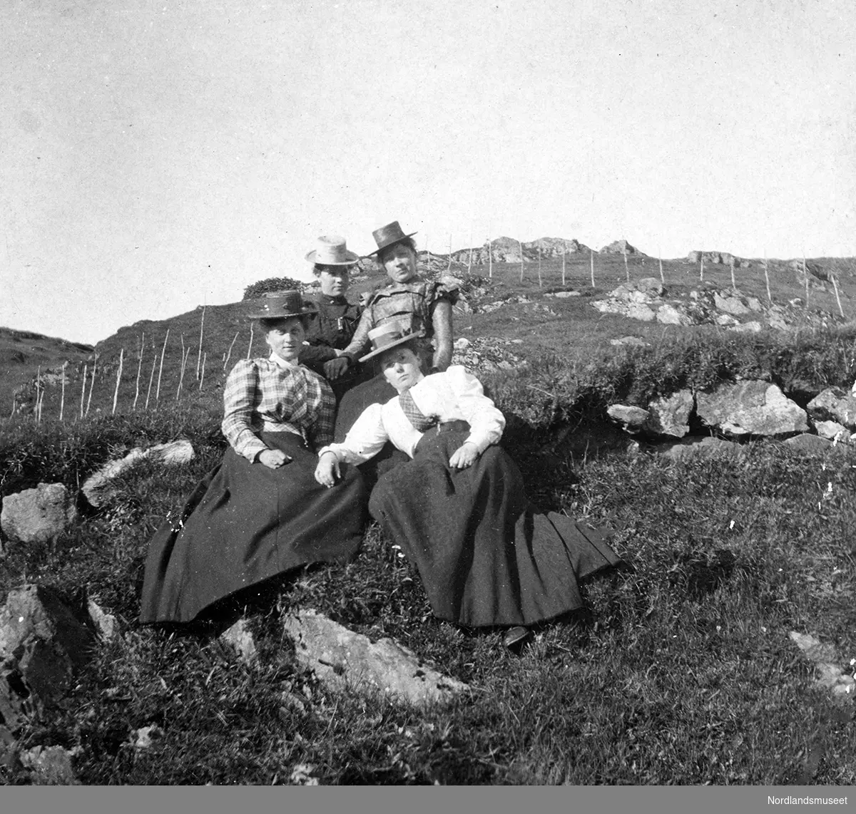 Fire kvinner med hatt slapper av ute i marka ved gården Fjellbirkeland, Bergen.