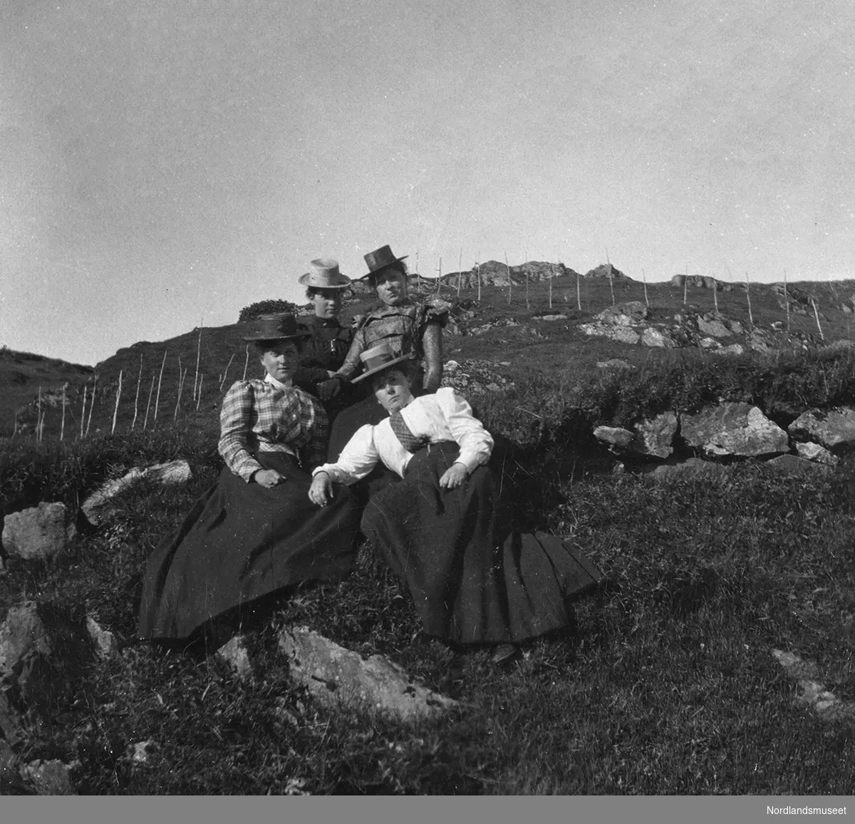 Fire kvinner med hatt slapper av ute i marka ved gården Fjellbirkeland, Bergen.