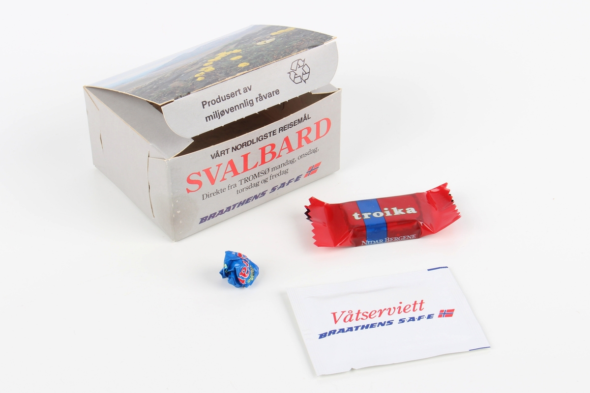 Eske fra servering om bord flyvning. Esken inneholder en våtserviett, en liten sjokoladebit og sjokoladepapir.
Med trykt annonse for en hotellkjede inni esken.