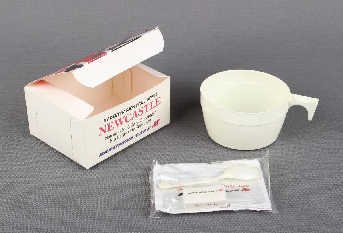 Eske fra servering om bord flyvning. Esken inneholder en kaffekopp og en liten pakke med serviett, melkepulver til kaffe/te, plastskje, og sukkerbit.