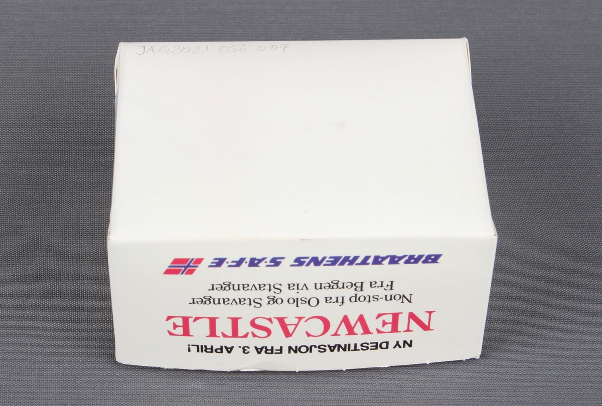 Eske fra servering om bord flyvning. Esken inneholder en kaffekopp og en liten pakke med serviett, melkepulver til kaffe/te, plastskje, og sukkerbit.