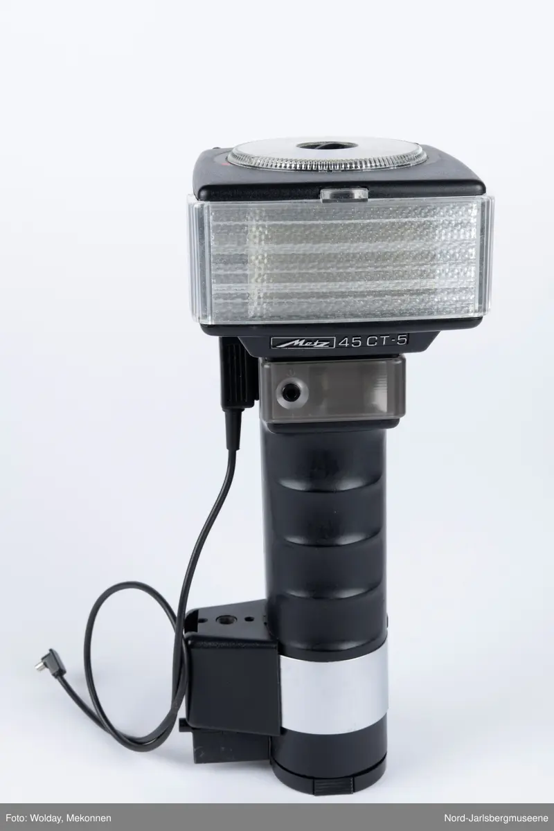 En sort blitlampe med skaft, løs ledning, uttakbart batteriinnsats nederst, på toppen en justerbar innstillingsskive i klarplast, har spredningsdeksel foran lampe