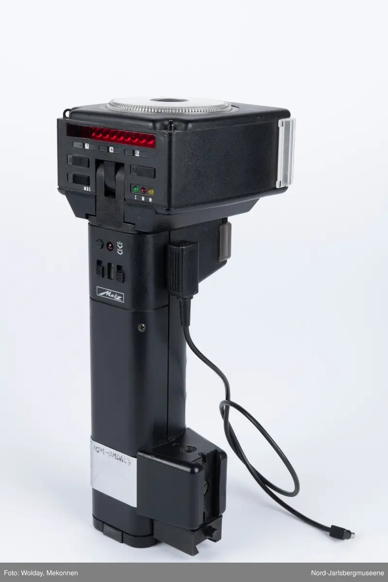 En sort blitlampe med skaft, løs ledning, uttakbart batteriinnsats nederst, på toppen en justerbar innstillingsskive i klarplast, har spredningsdeksel foran lampe