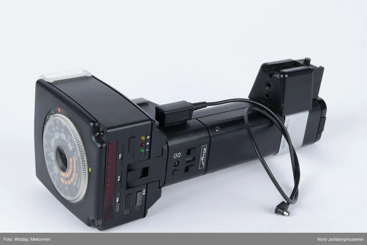 En sort blitlampe med skaft, løs ledning, uttakbart batteriinnsats nederst, på toppen en justerbar innstillingsskive i klarplast, har spredningsdeksel foran lampe