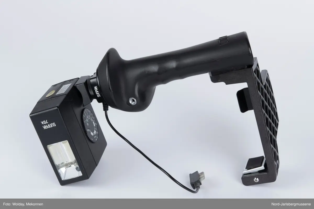 Sort kamerablitz, lysregusklering på siden av blitzhodet. ledning til kameratilkoblingsplugg fast. Er påmontert festebrakett (også Sunpak)