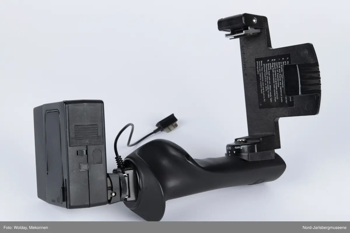 Sort kamerablitz, lysregusklering på siden av blitzhodet. ledning til kameratilkoblingsplugg fast. Er påmontert festebrakett (også Sunpak)