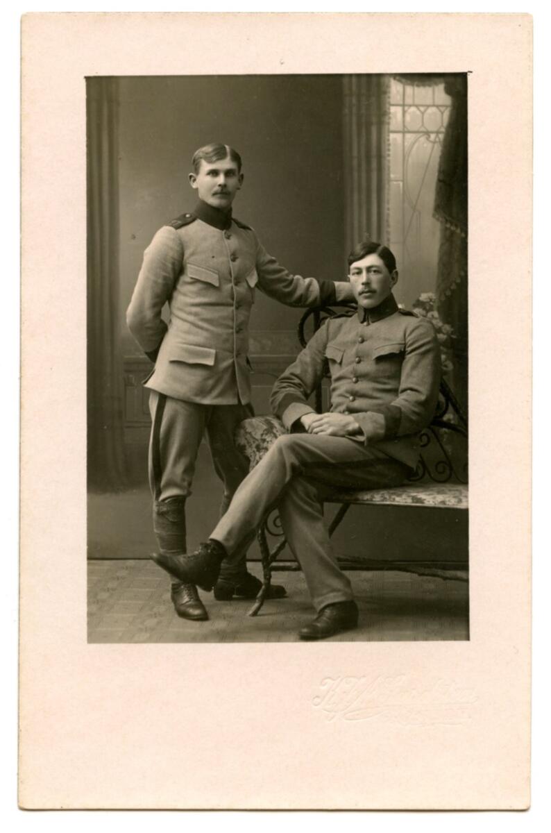 Vykort med svart-vitt fotografi av två män, taget i studio, troligtvis tidigt 1900-tal. Männen är klädda i uniform och poserar vid en stol, en sittande och den andra stående. Under fotografiet syns studions monogram i låg relief; "K. J. A. Gardsten, Wisby". Kortet är ej skrivet på. Ingen märkning på baksidan. Del av samling pappersmaterial från samma givare som donerades till museet år 1998.