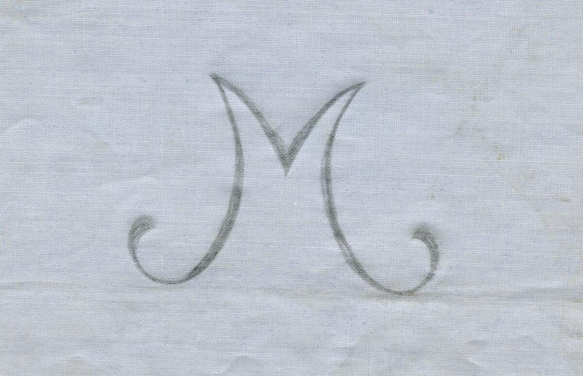 Broderimönster, ljusblått/grått papper, 11 st. i olika storlekar. Okänd ålder. Motiv: olika monogram; "M" och "MG" i olika varianter och konstellationer. Papperna något nötta, en del med permanenta veck efter att ha legat vikta under lång tid. Del av en samling textilmönster från samma donation, förvaras i en mapp (C25324_1).