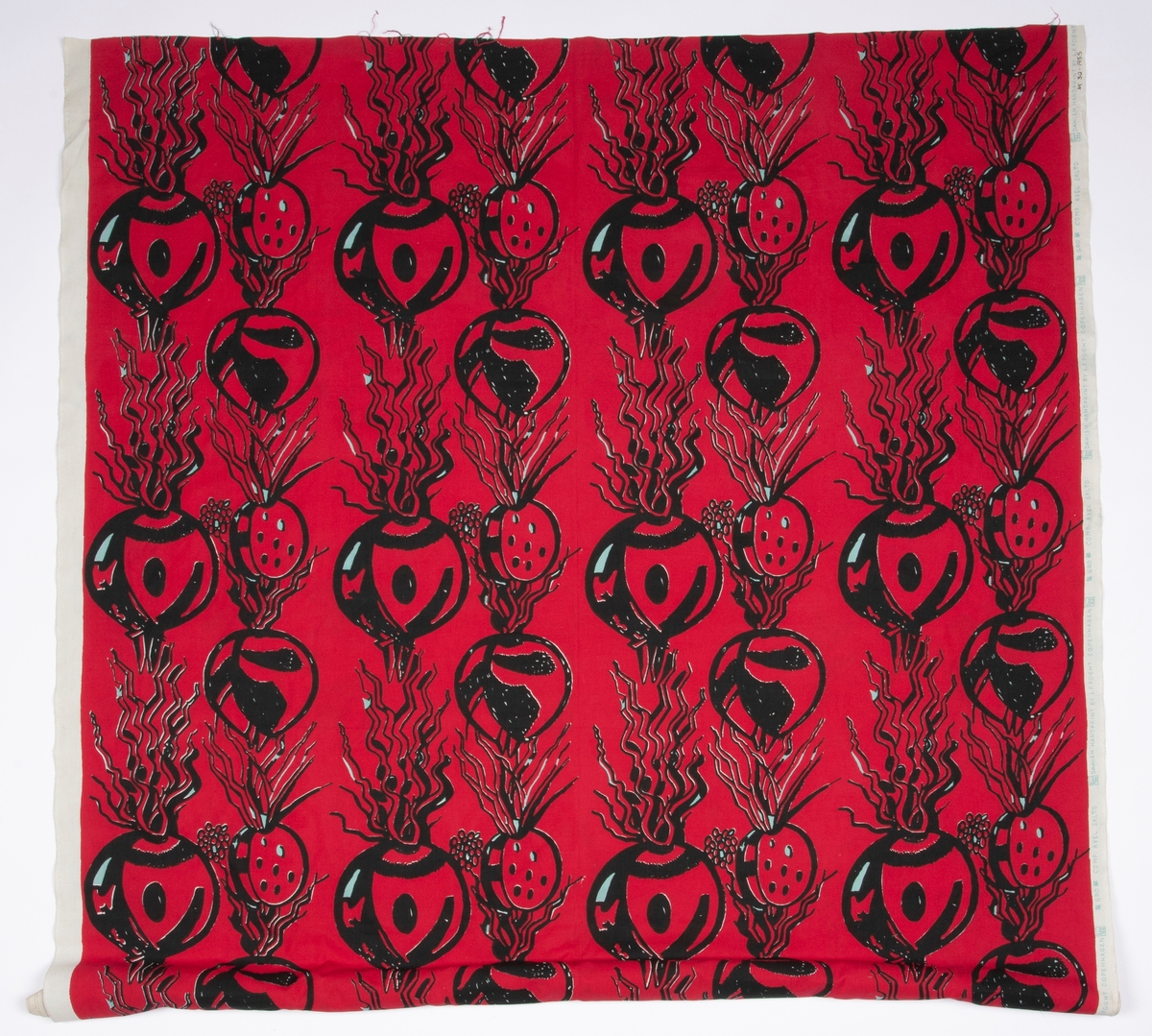 Håndtrykket mønstermotiv på vevd bomull. Stofftrykket er bortimot heldekkende mot det hvite bunnstoffet, med et motiv av røtter og spirer i sort med rød bakgrunn.