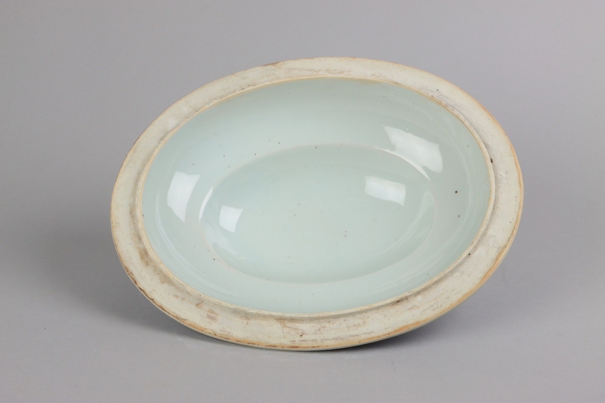 Oval shaped and slightly domed with knob in form of a flower head. On the top of lotus leaves and a list of pagoda lanscapes. The edge of the lid decorated with a dark blue  border in a criss cross pattern. All decor in blue underglaze. The inside of the lid is without decorations.