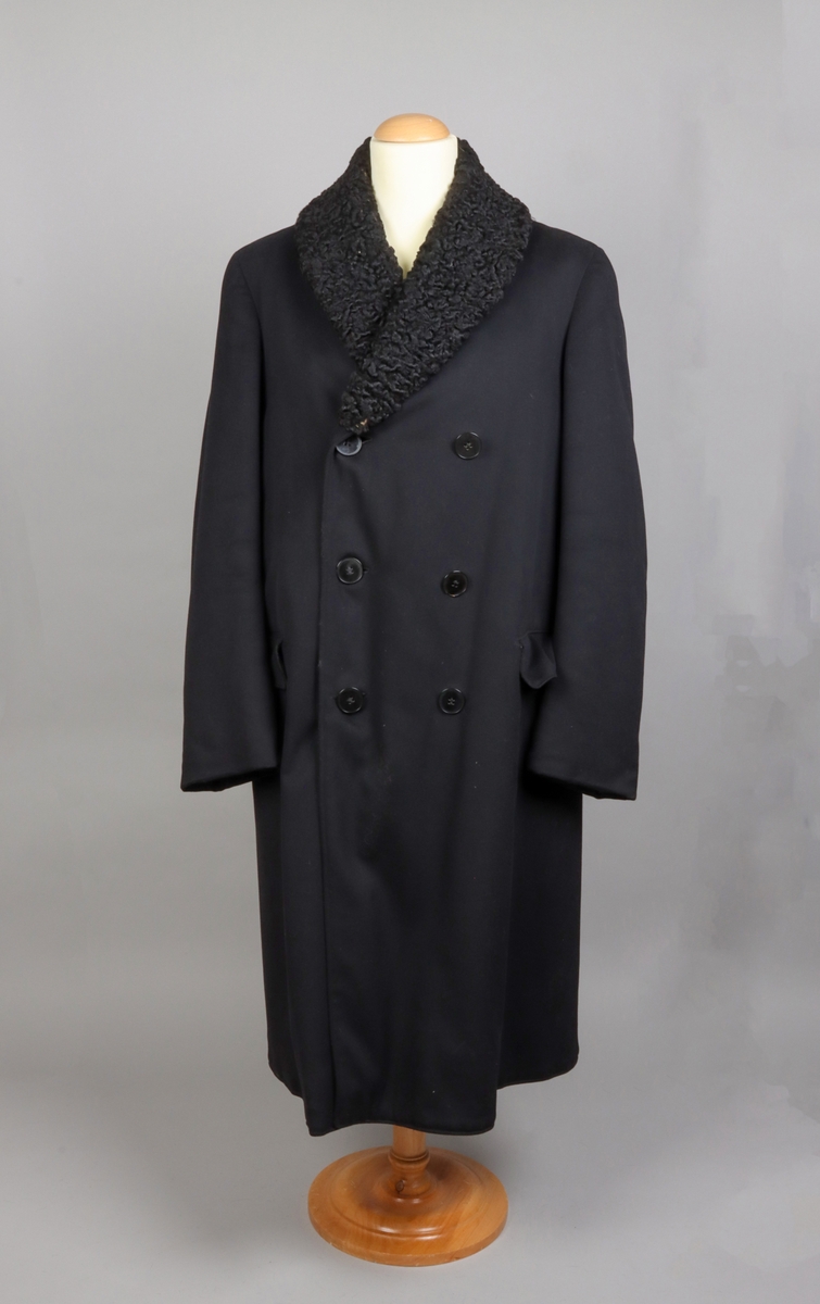 Rock av svart kläde fodrad med brun päls, troligen av bisamråtta. Ärmar fodrade med mörkbrunt fårskinn. Krages slag fodrade med svart persian. Rocken stängs med dubbelknäppning möjlig att knäppa åt båda håll. Sammanlagt sex svarta knappar. Två fickor med lock på framsidan. En innerficka prydd med namnskylt av silver.