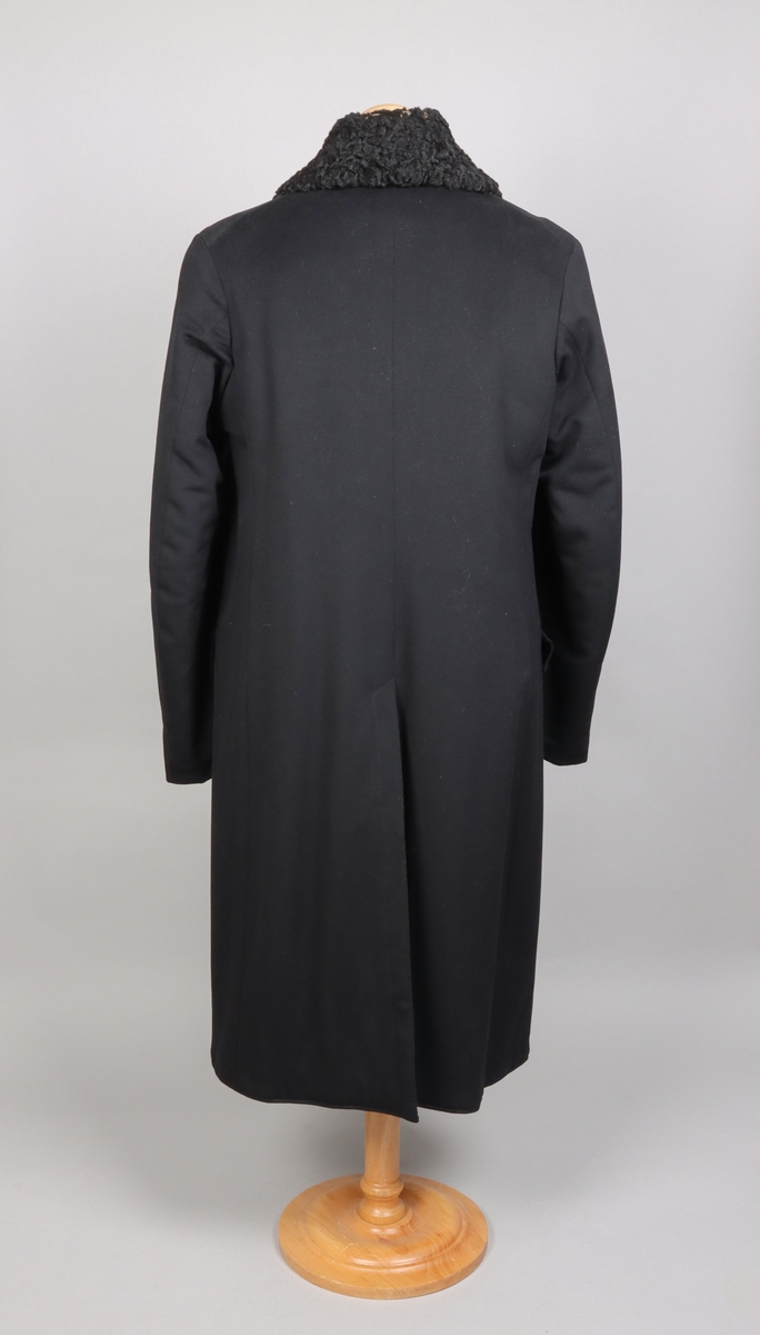 Rock av svart kläde fodrad med brun päls, troligen av bisamråtta. Ärmar fodrade med mörkbrunt fårskinn. Krages slag fodrade med svart persian. Rocken stängs med dubbelknäppning möjlig att knäppa åt båda håll. Sammanlagt sex svarta knappar. Två fickor med lock på framsidan. En innerficka prydd med namnskylt av silver.