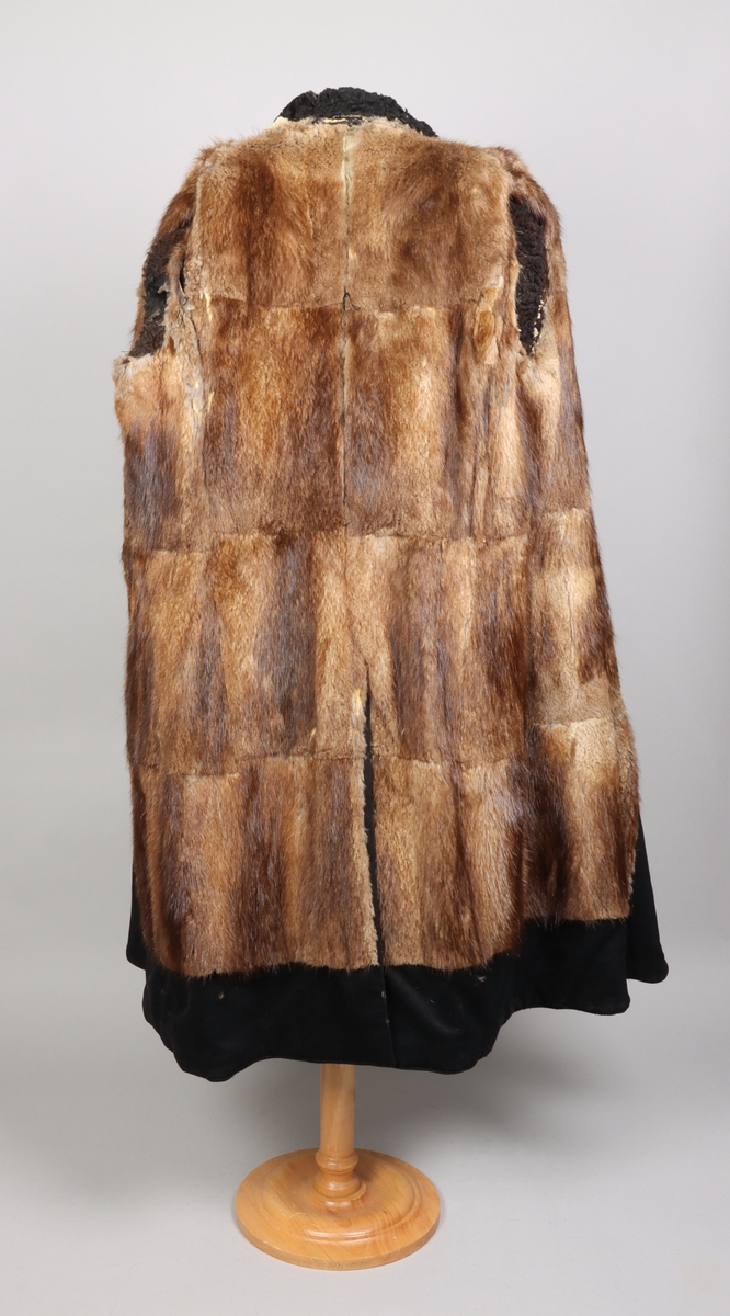 Rock av svart kläde fodrad med brun päls, troligen av bisamråtta. Ärmar fodrade med mörkbrunt fårskinn. Krages slag fodrade med svart persian. Rocken stängs med dubbelknäppning möjlig att knäppa åt båda håll. Sammanlagt sex svarta knappar. Två fickor med lock på framsidan. En innerficka prydd med namnskylt av silver.