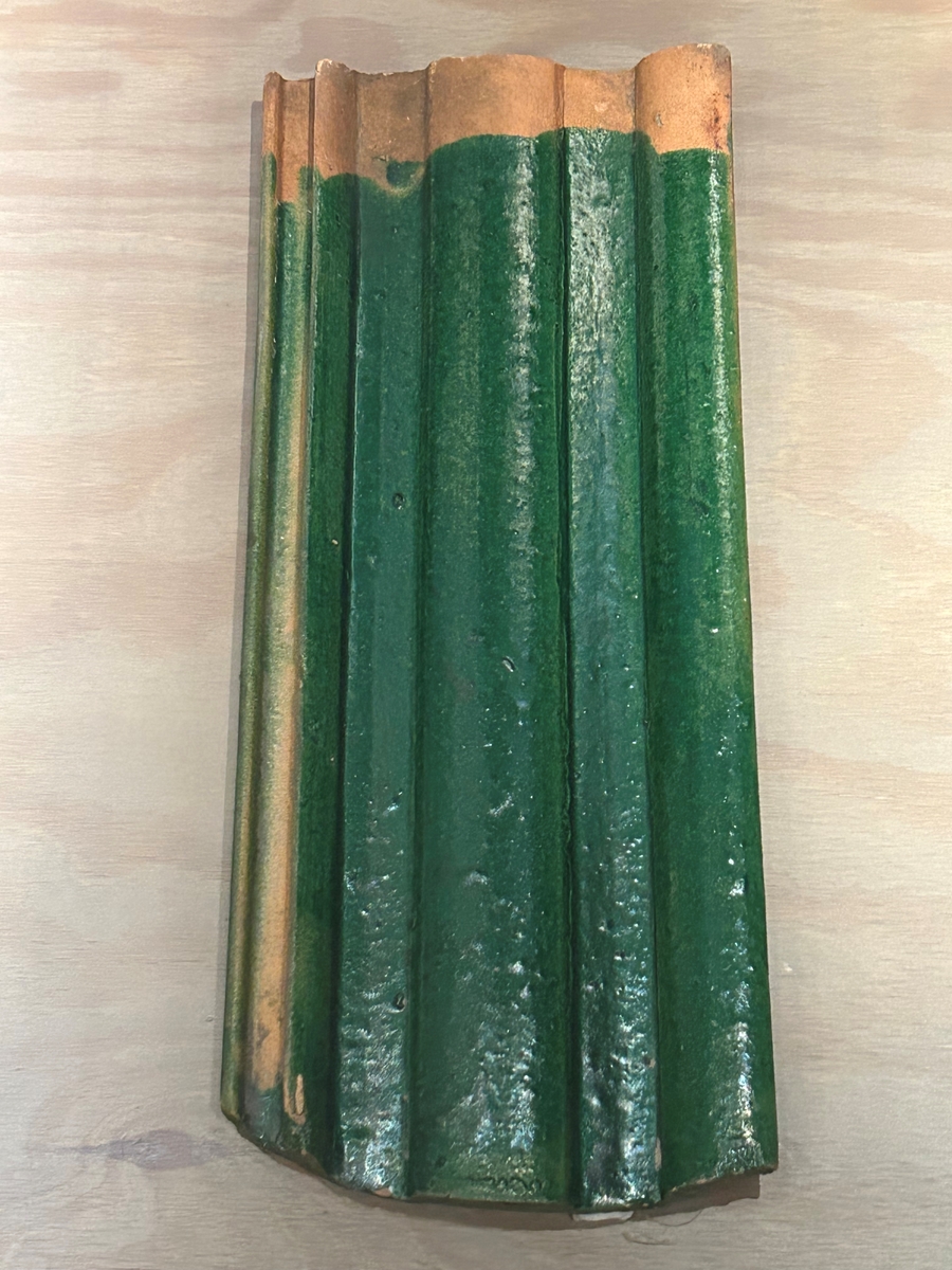 Falsat taktegel med grön glasyr på ovansidan. Glasyren sträcker sig över hela ytan sånär som på några centimeter från ena kortsidan, där nästa tegelpanna ska överlappa. Baksidan är oglaserad, med viss spillfärg i kanterna. På baksidan kan man också se teglet format med ett par "hakar" i övre änden, vilka ska läggas på takfoten vid monteringen.