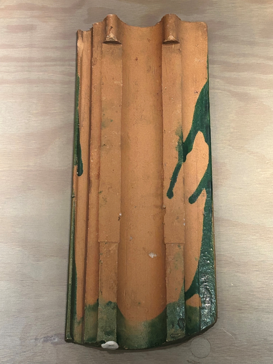 Falsat taktegel med grön glasyr på ovansidan. Glasyren sträcker sig över hela ytan sånär som på några centimeter från ena kortsidan, där nästa tegelpanna ska överlappa. Baksidan är oglaserad, med viss spillfärg i kanterna. På baksidan kan man också se teglet format med ett par "hakar" i övre änden, vilka ska läggas på takfoten vid monteringen.