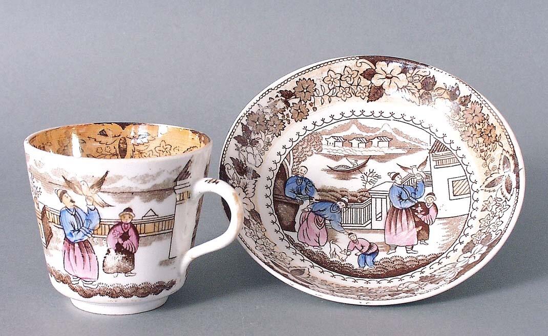 FRÅN GOTLANDS LANDSBYGD. INKÖP; ELIN PERSSON ANTIKHANDEL, VISBY.  KOPP: H. 7 CM, MYNN.DIAM. 8 CM. FAT H. 3 CM, DIAM. 14-15 CM. PORSLIN. VITA MED BRUNT TRYCK MÅLAT I RÖTT, BLÅTT OCH GUDLYSTER (GULT) KINESISKT MOTIV.  KOPPEN: TERASS MED MÄNNISKOR, VUXNA OCH BARN., LEKANDE MED EN HUND OCH EN FÅGEL. EN DEL AV ETT HUS SKYMTAR VID ÖRAT, SJÖUTSIKT MED HUS OCH BERG SAMT EN BÅT. INSIDAN VID MYNNINGEN FÖRSEDD MED BLOMBÅRD MED BL.A NYPONROSOR OCH TREDELADE BLAD. FATET: PÅ BRÄTTET SAMMA MOTIV SOM PÅ KOPPENS INSIDA. I BOTTEN SAMMA MOTIV SOM PÅ KOPPENS UTSIDA MEN SAMMANDRAGET. PS. 882: KOPPARNA FÖRSEDDA MED MÅLAT krYSS, FATEN MED "19". ETT FAT ÄVEN FÖRSETT MED krYSS (MÅLAT).  (1870-80, A. BLOCK). ( ÖSTERSTUGAN, NORRA VÄGGEN I PS. 848 ).