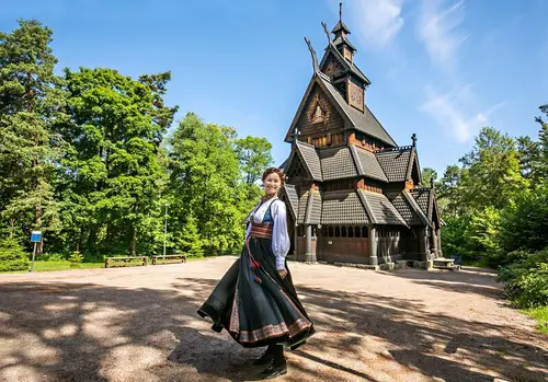 Woman in traditional Norwegian costume standing in front of the Gol Stave Church at the Open-Air Museum at Norsk Folkemuseum.