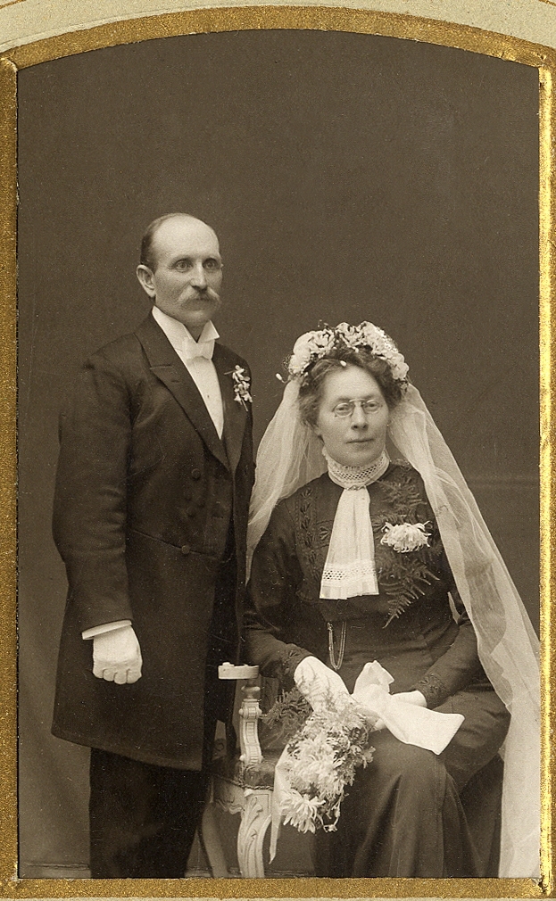 Okänt brudpar hos fotografen. Han i bonjour, hon i mörk brudklänning med vit s.k. jabot. m.m..