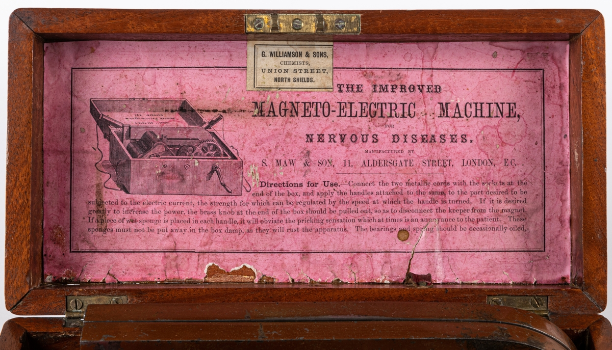 Magnetisk-elektrisk maskin för nervösa sjukdomar. Tillverkad av S.MAW & SON, II ALDERSGATE STREET, LONDON, EC. I en trälåda med mahognyfanér två hästskomagneter, sammetsklädd rotor samt ställning och kugghjul av mässing. Två elektriska poler fästes på lådans kortsidor. En mässingsvev med svart handtag skruvas fast på framsidan.