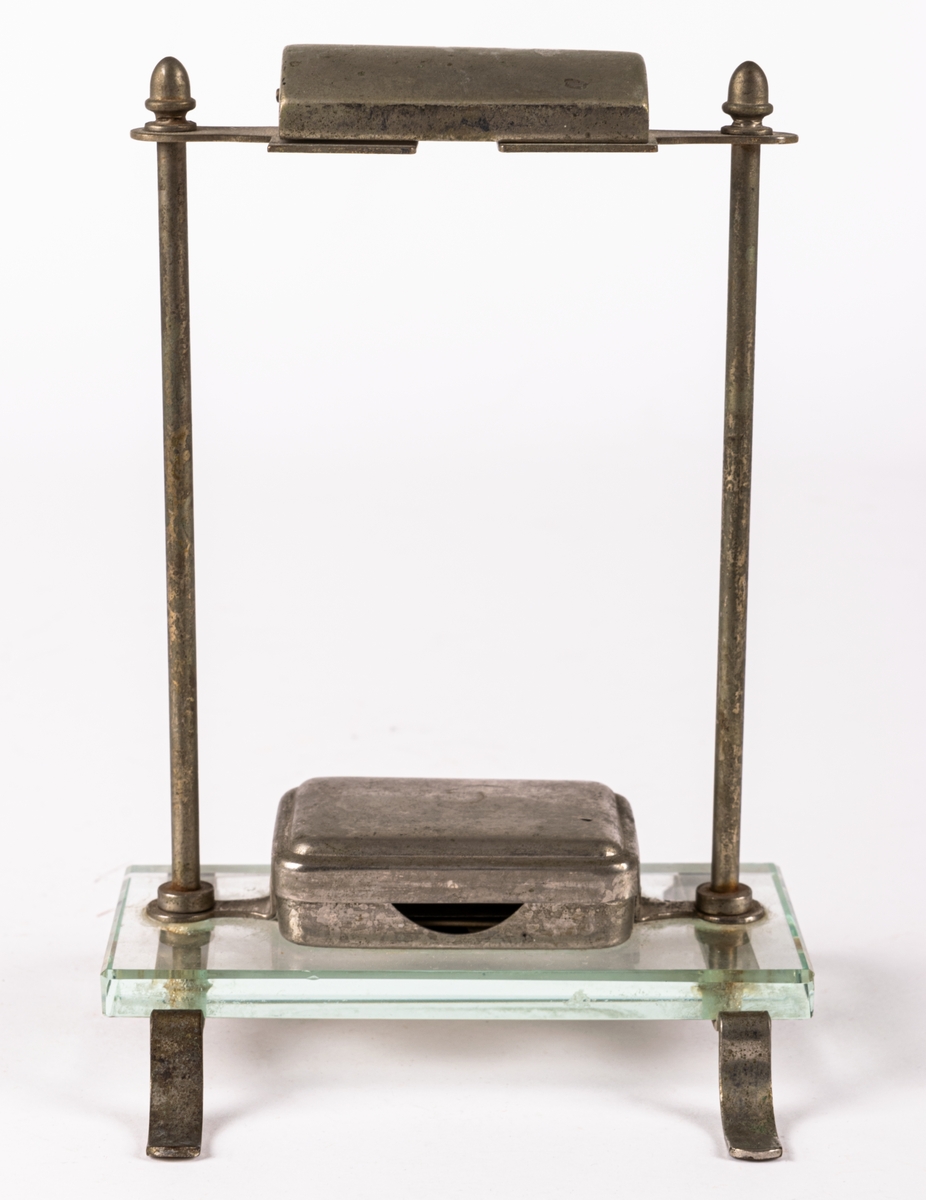 Ställ för rakhyvel. Ställning, skydd för rakhyvel och ask för rakblad i metall. På benen i metall en rektangulär glasskiva på vilken rakbladsasken står. 12 rakblad ingår. Rakbladen märkta SWING, DRABANT, MATADOR 25, GILETTE och MATADOR NATIONAL BLÅ.