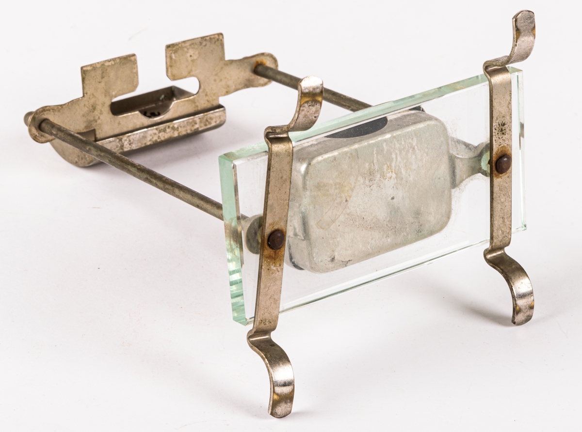 Ställ för rakhyvel. Ställning, skydd för rakhyvel och ask för rakblad i metall. På benen i metall en rektangulär glasskiva på vilken rakbladsasken står. 12 rakblad ingår. Rakbladen märkta SWING, DRABANT, MATADOR 25, GILETTE och MATADOR NATIONAL BLÅ.