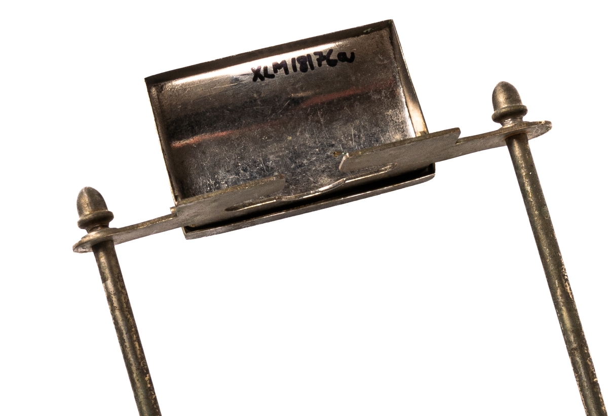 Ställ för rakhyvel. Ställning, skydd för rakhyvel och ask för rakblad i metall. På benen i metall en rektangulär glasskiva på vilken rakbladsasken står. 12 rakblad ingår. Rakbladen märkta SWING, DRABANT, MATADOR 25, GILETTE och MATADOR NATIONAL BLÅ.