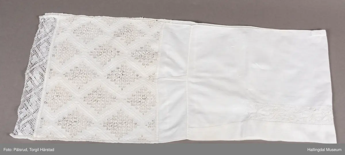 Den ene langsides midtparti har innefor bred fald, bord av 3 rosetter og 7 sløyfelignende ornamenter. Kortsidene er kantet med knipling og prydet med et bredt parti av ruter i hardangersøm. Hodkluten er ved tverrsømmer sammensatt av 5 forskjellige deler. Endestykkene med hardangersømmen er av grovere tøy enn det øvrige. 
 R.B.S.
