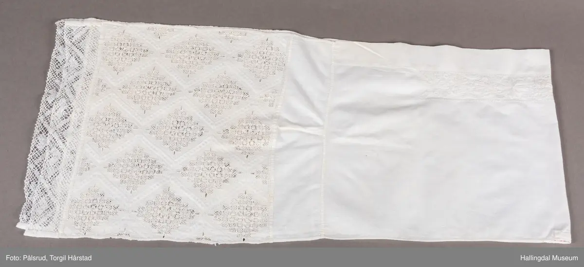 Den ene langsides midtparti har innefor bred fald, bord av 3 rosetter og 7 sløyfelignende ornamenter. Kortsidene er kantet med knipling og prydet med et bredt parti av ruter i hardangersøm. Hodkluten er ved tverrsømmer sammensatt av 5 forskjellige deler. Endestykkene med hardangersømmen er av grovere tøy enn det øvrige. 
 R.B.S.