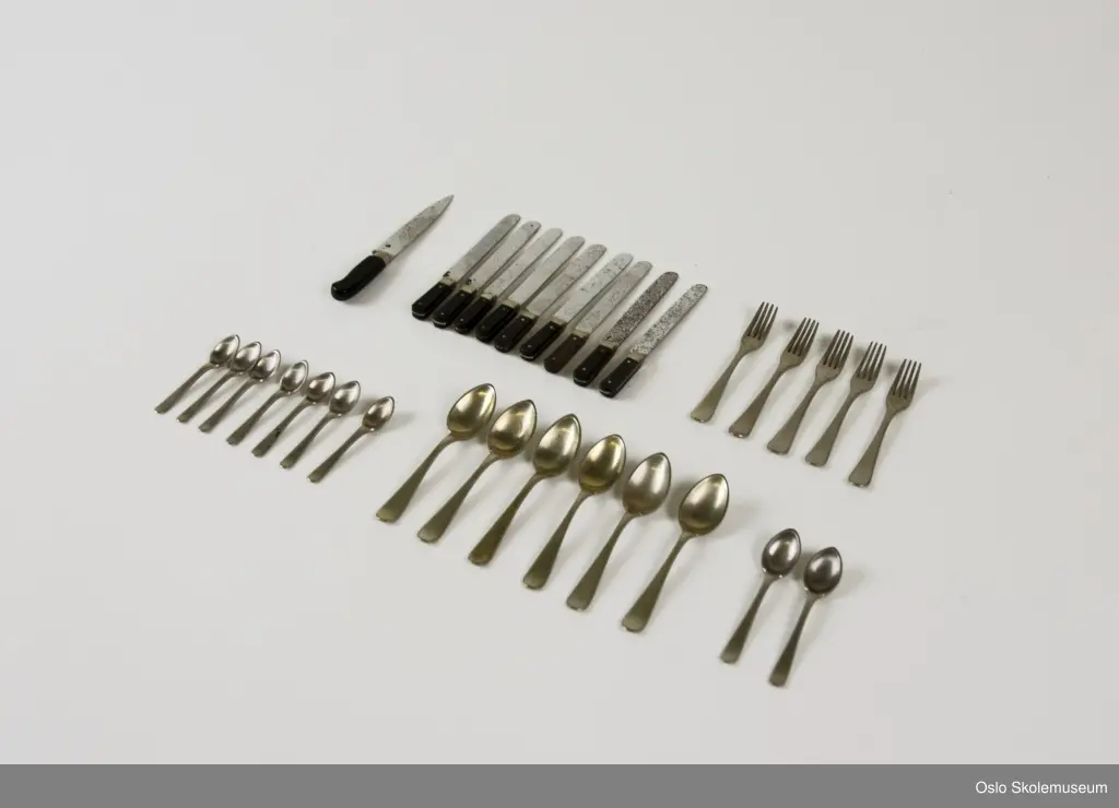 Bestikksett bestående av 30 deler. Det er ni kniver, fem gafler, sju teskjeer, to spiseskjeer, seks serveringsskjer og en skjærekniv. Knivene har svartmalt skaft.