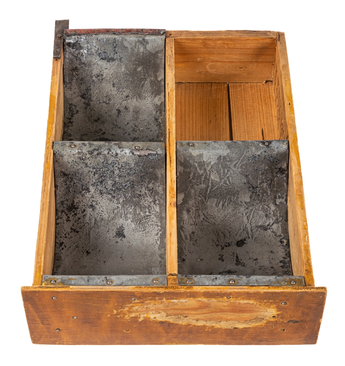 Låda av trä och plåt. Själva lådan är ihopspikad av tunna brädor vilka synes ha sågats ur en större låda för frakt el. dyl. Ljusa brädor. Framsidan av lådan är något bredare än resten: 225mm. Lådan är genom brädväggar indelad i fyra fack. De två främre något större än de bakre. Tre av facken (ej det höger bak) är klätt i plåtband, lika breda som facken, dock ej sidoväggarna i facken. Plåten följer inte fackens former utan går bara i en båge ned i facken. På brädorna inuti lådan kan man i brunt läsa "MUSTAD" och "MA GARIN"- troligen ett "R" täckt av avdelning av väggarna. Även på lådans undersida står "MUSTAD" undersidan är spikad av två brädor, en smal och en bred med ca 1/2cm glapp emellan. Ca 2/4 delar av lådans ytterkanter målade i gult. Framsidan målad brun men färgen borta i en fläck.