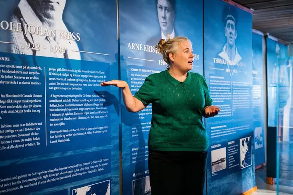 En dame peker og forteller foran plakater for sjøfart