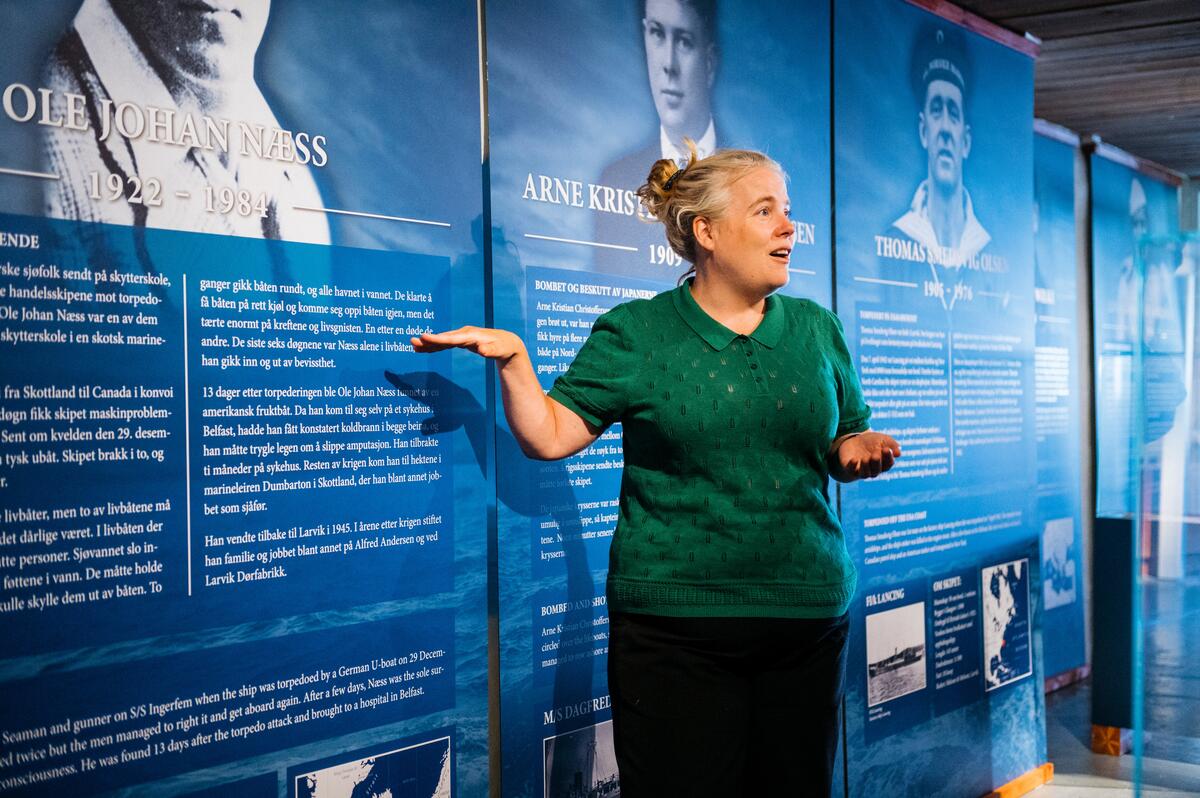 En dame peker og forteller foran plakater for sjøfart