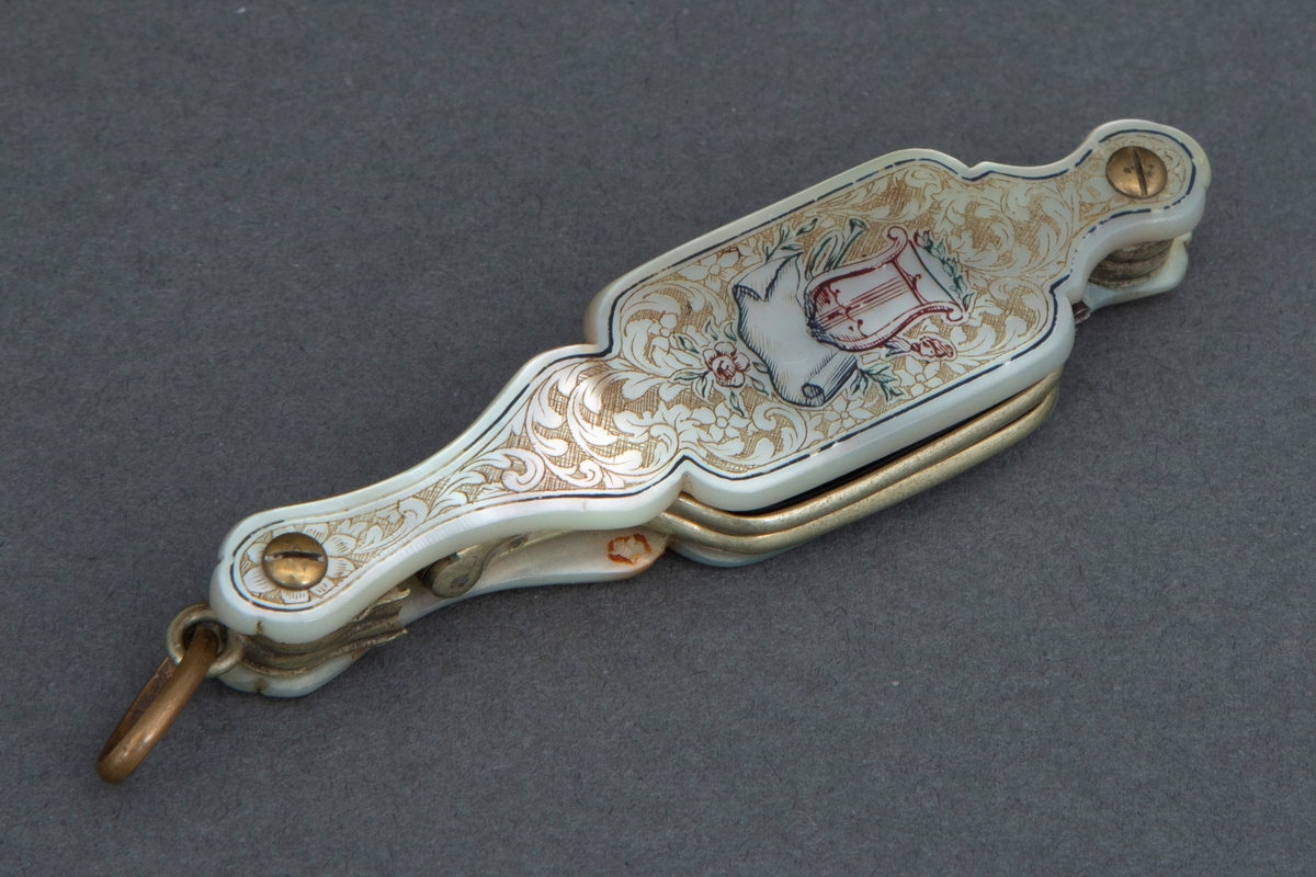 Sammenleggbar stanglorgnett i perlemorsholder. Holderens yttersider er dekorert med innrissede akantusblader på skrafert bunn og med en lyre i midten. Selve brillene er innfattet i en tynn rektangulær metallramme med avrundede hjørner. Glasset er dyptgrønt. Brillene kan ved et fjærende midtledd legges dobbelt før de skyves inn i holderen.