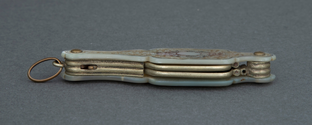 Sammenleggbar stanglorgnett i perlemorsholder. Holderens yttersider er dekorert med innrissede akantusblader på skrafert bunn og med en lyre i midten. Selve brillene er innfattet i en tynn rektangulær metallramme med avrundede hjørner. Glasset er dyptgrønt. Brillene kan ved et fjærende midtledd legges dobbelt før de skyves inn i holderen.