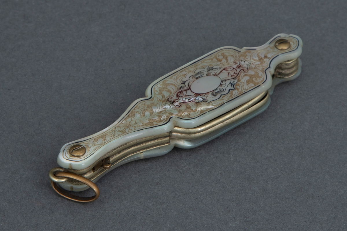 Sammenleggbar stanglorgnett i perlemorsholder. Holderens yttersider er dekorert med innrissede akantusblader på skrafert bunn og med en lyre i midten. Selve brillene er innfattet i en tynn rektangulær metallramme med avrundede hjørner. Glasset er dyptgrønt. Brillene kan ved et fjærende midtledd legges dobbelt før de skyves inn i holderen.