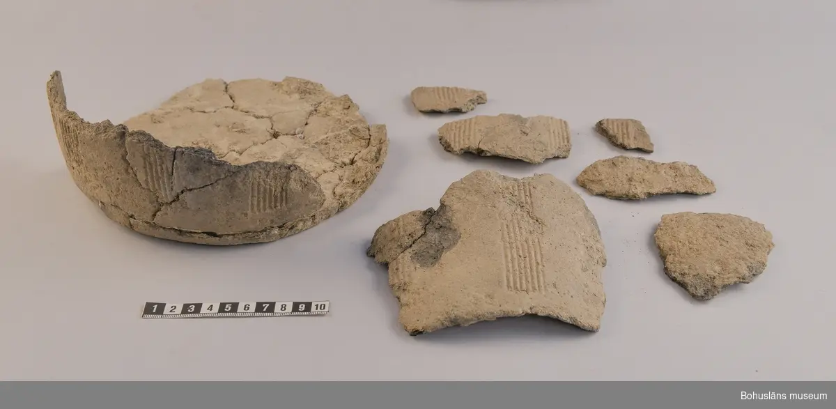 Osäkert antal bitar, många mindre bitar oräknade. Kärlets botten delvis ihoplimmat. Bottendiam: 20 cm.
Fyndnumret innehåller även ett par bitar ordinärt rödbränt lergods.