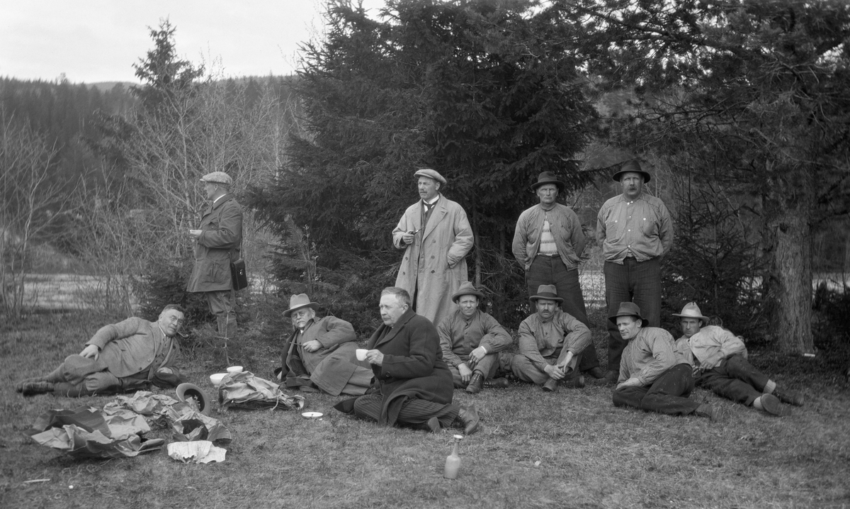 Direksjonen i Christiania Tømmerdirektion (seinere Glomma fellesfløtingsforening) på befaring langs vassdraget i 1927.  Her er de samlet på ei grasslette i Stor-Elvdal, antakelig i nærheten av elva Søkkundas utløp på Glommas vestside litt sør for Rasta.  Dem menn fra fløtingsstyret nyter kaffe, to i stående posisjon og tre i hvilende posisjoner på bakken, til venstre i bildet.  Disse mennene skiller seg, med sine frakker og dresser, tydelig fra de busserullklede fløterne til høyre i bildet.  Blant fløterne synes vi å dra kjensel på Thorvald Øyen og Kristian Øyen, stående bakerst til høyre på bildet.
