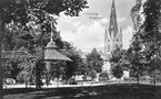 Vykort med utblick över parken invid Borggården i Linköping. Närmast ses den musikpaviljong som kom till vid 1900-talets början. I fonden stadens slott och stiftets domkyrka.