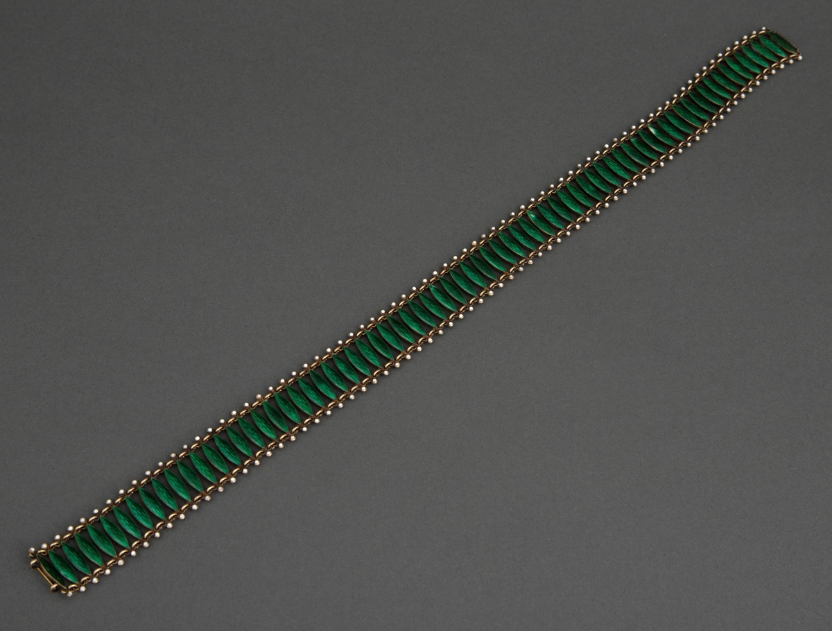 Halsband satt sammen av 72 tverrstaver dekket av grønn, halvtransparent emalje over guillochering. Leddenes form er spissoval med trepassformet utvidelse ved hver ende med huller for bøyler som holder leddene sammen og ytterst en "perle" i hvit emalje. Bakside og bøyler er av forgylt sølv. Hektelås til lukking av smykket.