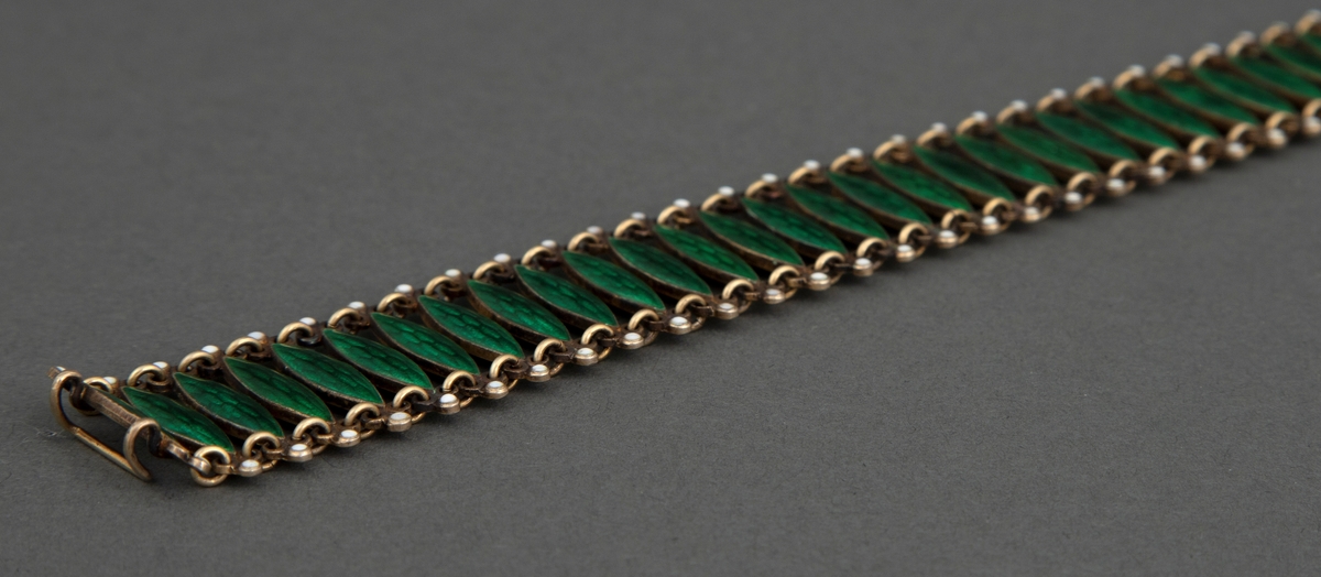 Halsband satt sammen av 72 tverrstaver dekket av grønn, halvtransparent emalje over guillochering. Leddenes form er spissoval med trepassformet utvidelse ved hver ende med huller for bøyler som holder leddene sammen og ytterst en "perle" i hvit emalje. Bakside og bøyler er av forgylt sølv. Hektelås til lukking av smykket.