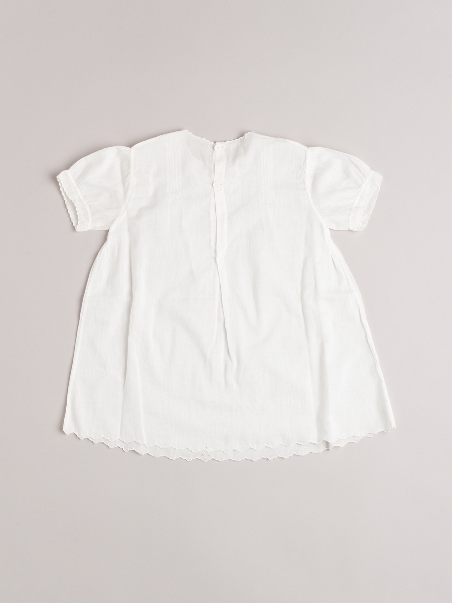 Kjole med underkjole i helt tynn bomull. Håndsydd. Broderte tungekanter langs alle kanter/åpninger. Smale biser og broderi på kjolens forstykke.
Baby- og barnetøy som først var brukt av tre søstre i USA på 1930- og 40-tallet, før det ble sendt til Norge og brukt av tre søstre i Eidsberg på 1940- og 50-tallet - kusiner av de tre i USA.