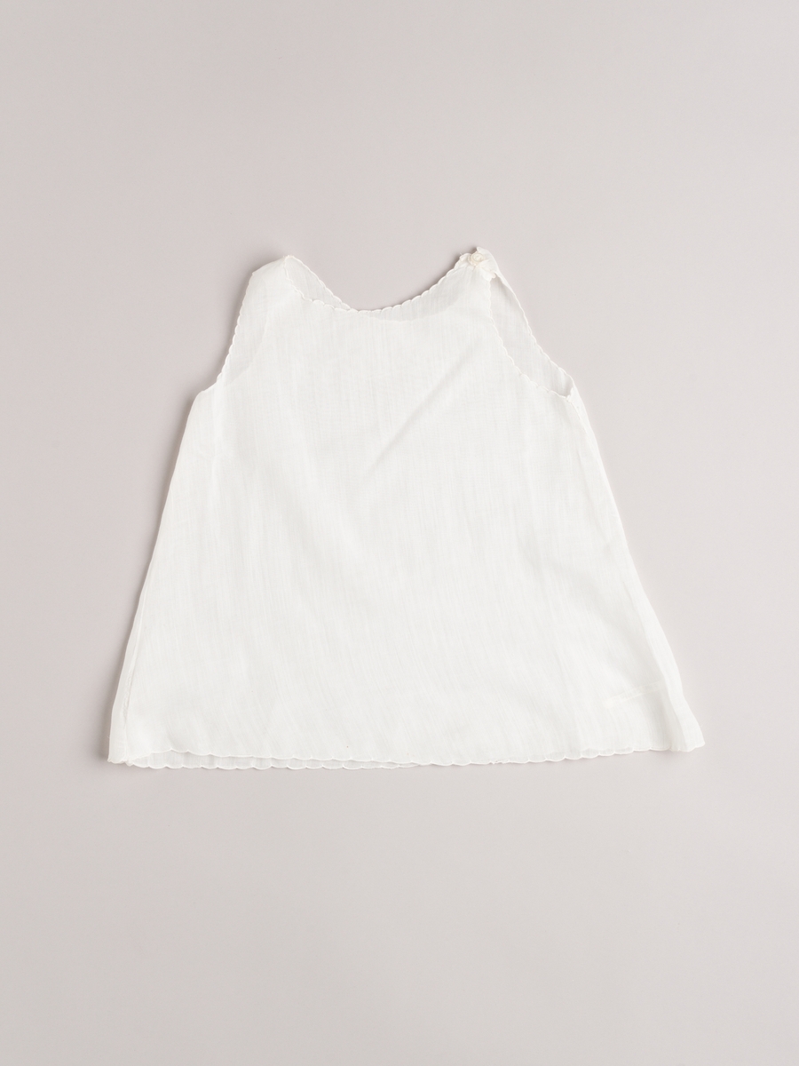 Kjole med underkjole i helt tynn bomull. Håndsydd. Broderte tungekanter langs alle kanter/åpninger. Smale biser og broderi på kjolens forstykke.
Baby- og barnetøy som først var brukt av tre søstre i USA på 1930- og 40-tallet, før det ble sendt til Norge og brukt av tre søstre i Eidsberg på 1940- og 50-tallet - kusiner av de tre i USA.