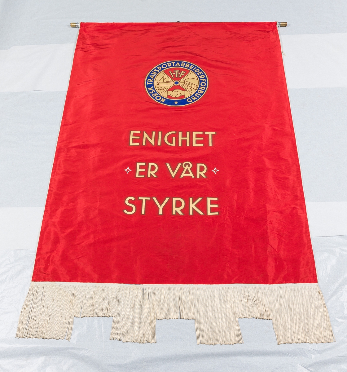 Blå fane med midtstilt motiv av skip ved kai. Rød fanekappe. Faneduken er montert på tverrstang med toppsyd og sidespyd. Bærestang.