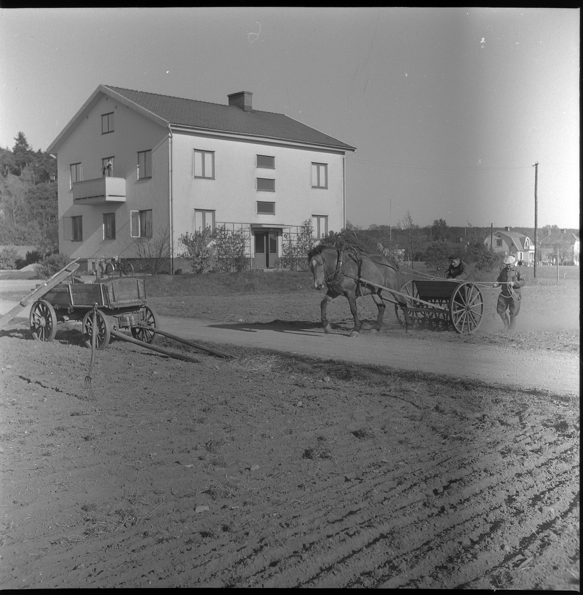 Två män med häst utför jordbruksarbete utanför fastighet nedan Häradsberget, Boråsvägen. Idag är byggnaden riven. Maj 1950.