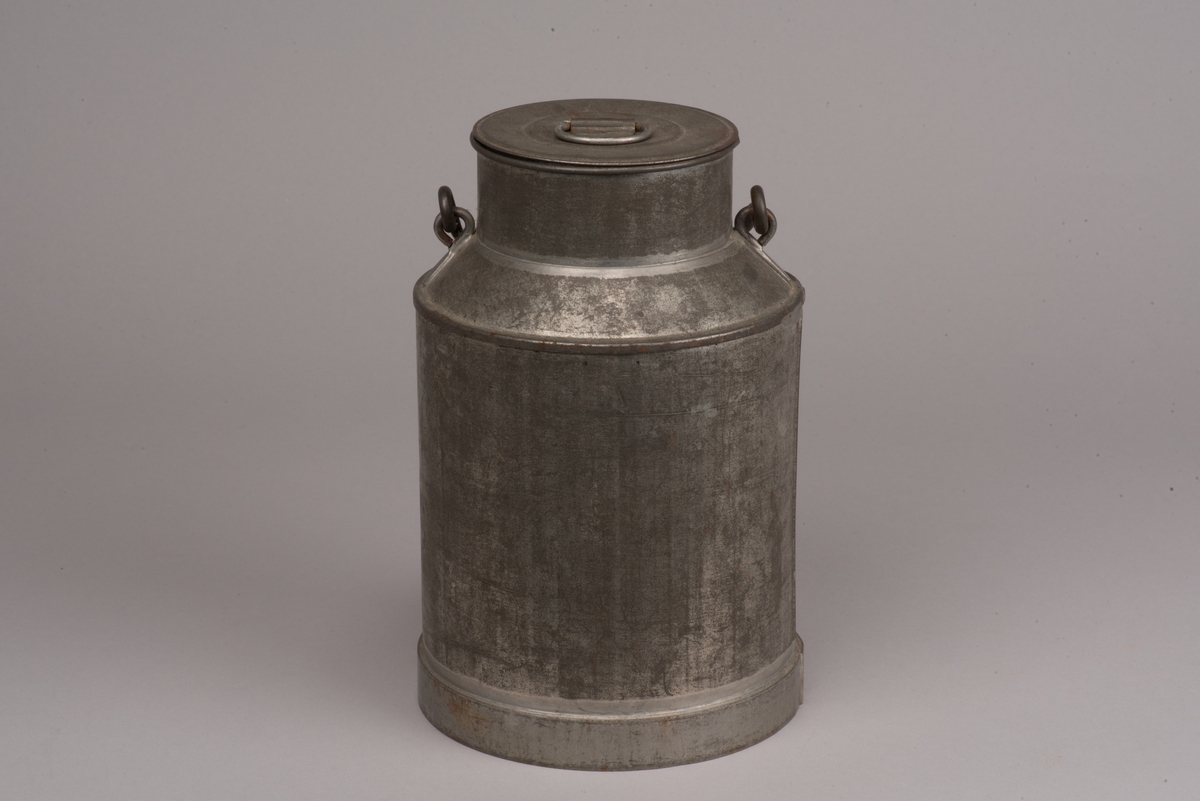 Cylindrisk mjölkanna med lock av bleckplåt.
Den avsmalnade halsen är försedd med ett bygelhandtag i stål. Även locket har ett pålött handtag.