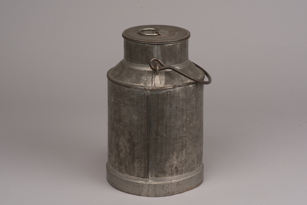 Cylindrisk mjölkanna med lock av bleckplåt.
Den avsmalnade halsen är försedd med ett bygelhandtag i stål. Även locket har ett pålött handtag.