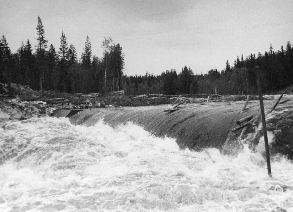 Tømmerfløting i elva Søndre Osa i Åmot kommune i Hedmark. Fotografiet er tatt våren 1936, ved den da nybygde kraftverksdammen ved Kvernfallet. I forgrunnen ser vi hvordan vannet og tømmerstokkene fløt over den avrundete damkrona. Den underliggende konstruksjonen, som vi ikke ser på dette bildet, var utført i armert betong. Bildeter tatt fra søndre elvebredd, skrått mot dammen. 

I 1936 var det innmeldt 383 088 tømmerstokker til fløting fra Osensjøen og tilflytende vassdrag. 28 prosent av stokkene ble levert ved Slemma, 10 prosent ved Nordre Osa, 7 prosent ved Brøa, 13 prosent ved Ena med Ulvsjøvassdraget, 7 prosent ved Tverrena og resten, 35 prosent, ble levert ved Osensjøens strender. Alt dette tømmeret. pluss noe av et kvantum på 72 506 stokker som var levert ved Søndre Osa, skulle passere den nye kraftverksdammen ved Kvernfallet. Aktørene i fløtinga var naturlig nok spente på om dammen kom til å bli et hinder der stokkene satte seg fast på eller like nedenfor dammen. Det skjedde ikke. Kvernfalldammen kom ikke til å skape nevneverdige problemer for tømmerfløtinga.