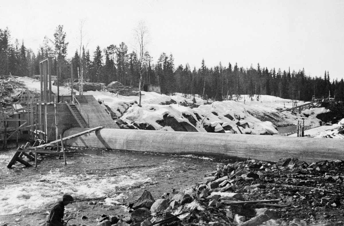 Bygging av terskeldam ved Kvernfallet i elva Søre Osa i Åmot kommune i Hedmark våren 1936. Fotografiet er tatt fra nordre elvebredd, skrått i medstrøms retning. I forgrunnen ser vi den avrundete damterskelen, utført i armer betong, som var støpt på tvers av elveløpet med vanninntak for turbinrøret ved søndre elvebredd (til venstre på dette fotografiet) der elveløpet var djupest. På den fortsatt snødekte elvebrinken lå det forskalingsmaterialer. Sjølve kraftstasjonen ble lagt ved Brufallet, noen hundre meter lenger sør.