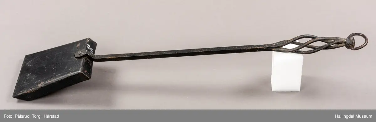 En pesspade eller askespade i smijern med vridd håndtak med ring i enden.